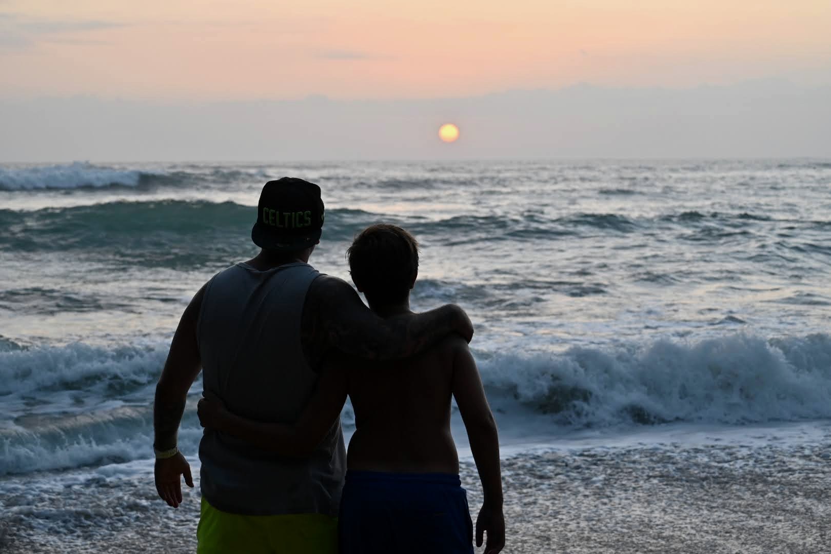 Enrique y su hijo de espaldas, abrazados, mirando la puesta de sol frente al mar