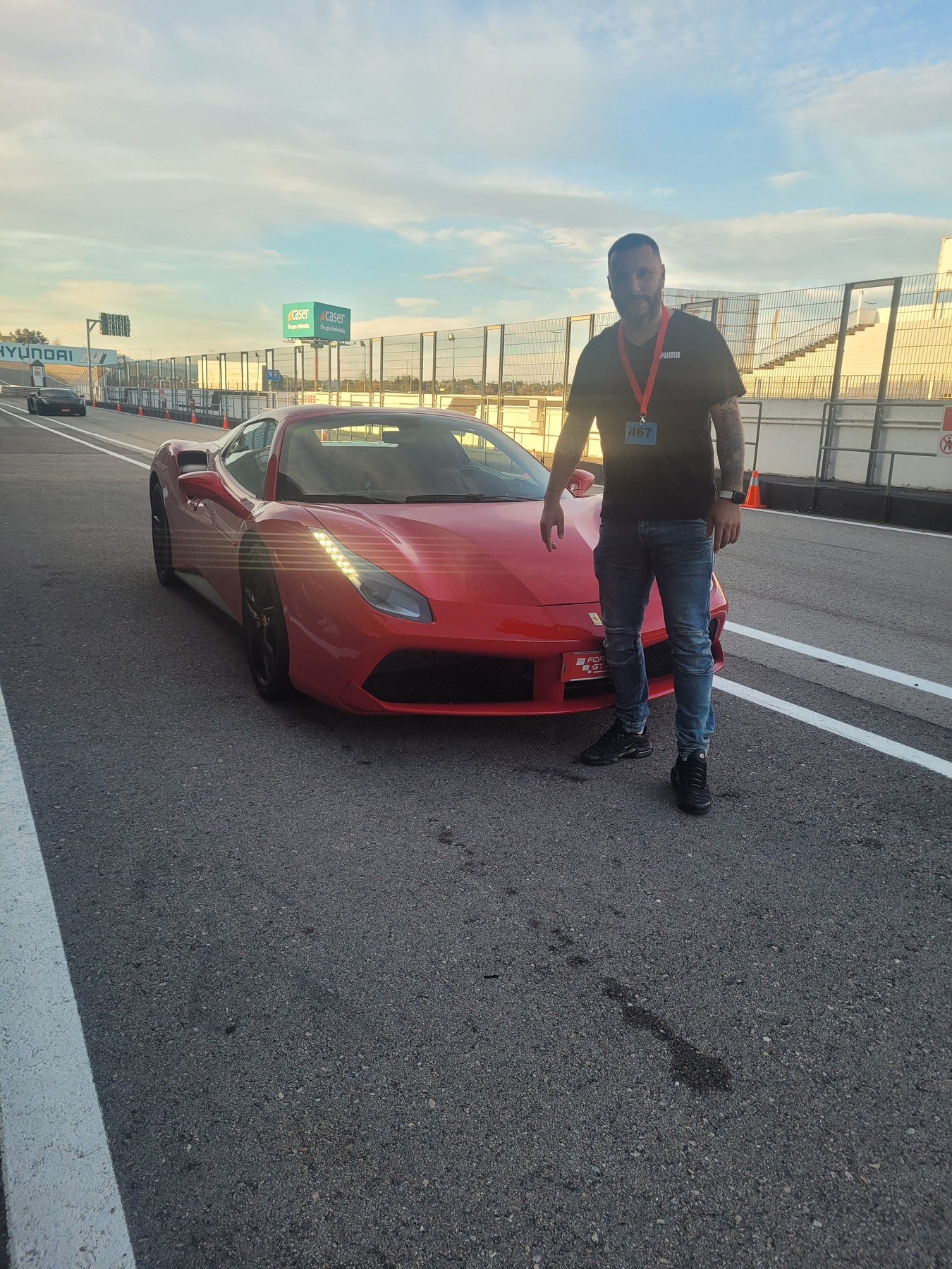 Enrique junto a un Ferrari en un circuito, tarde soleada