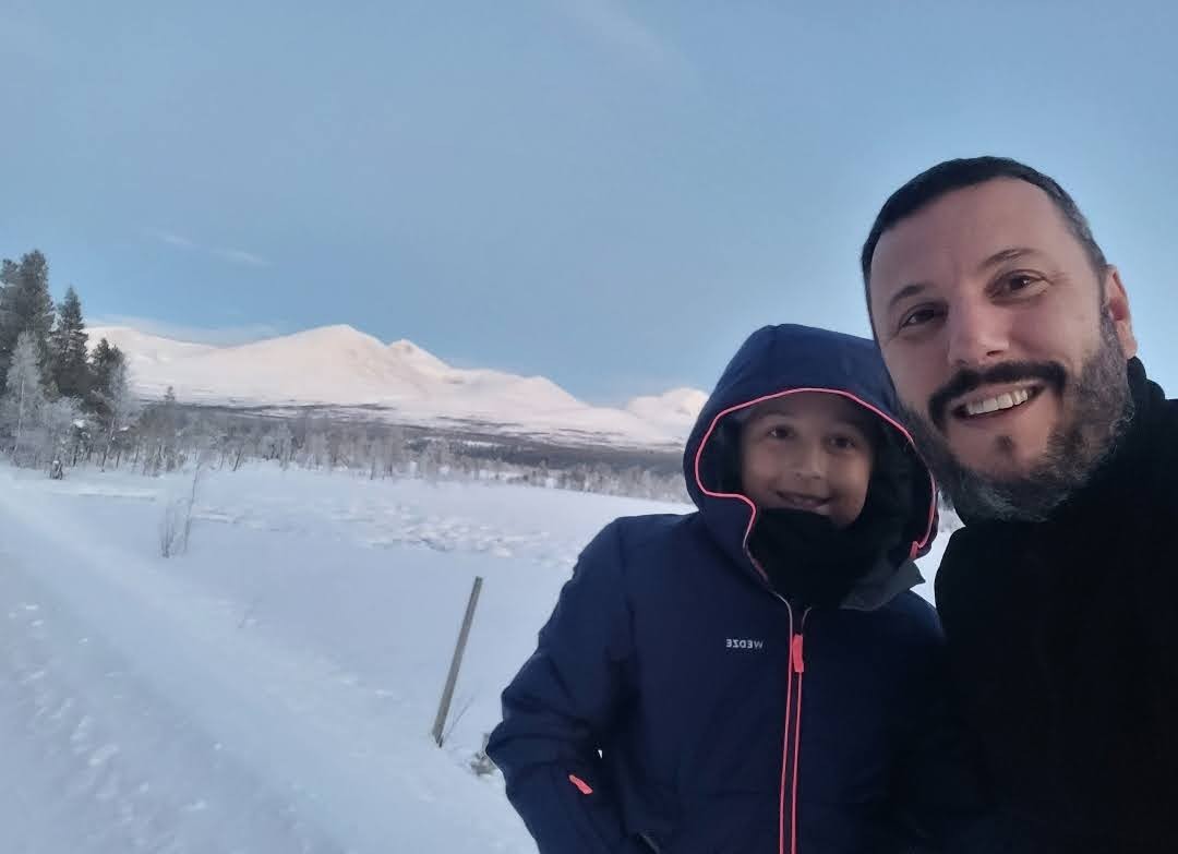 Enrique con su hijo, sonriendo, en un paisaje nevado con montañas al fondo